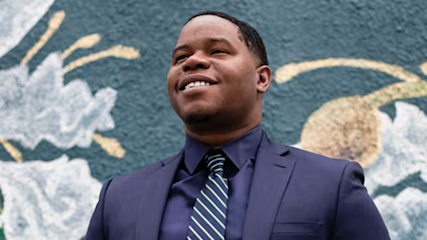 Professional in navy suit and striped tie smiling confidently against colorful wall mural with abstract cloud designs